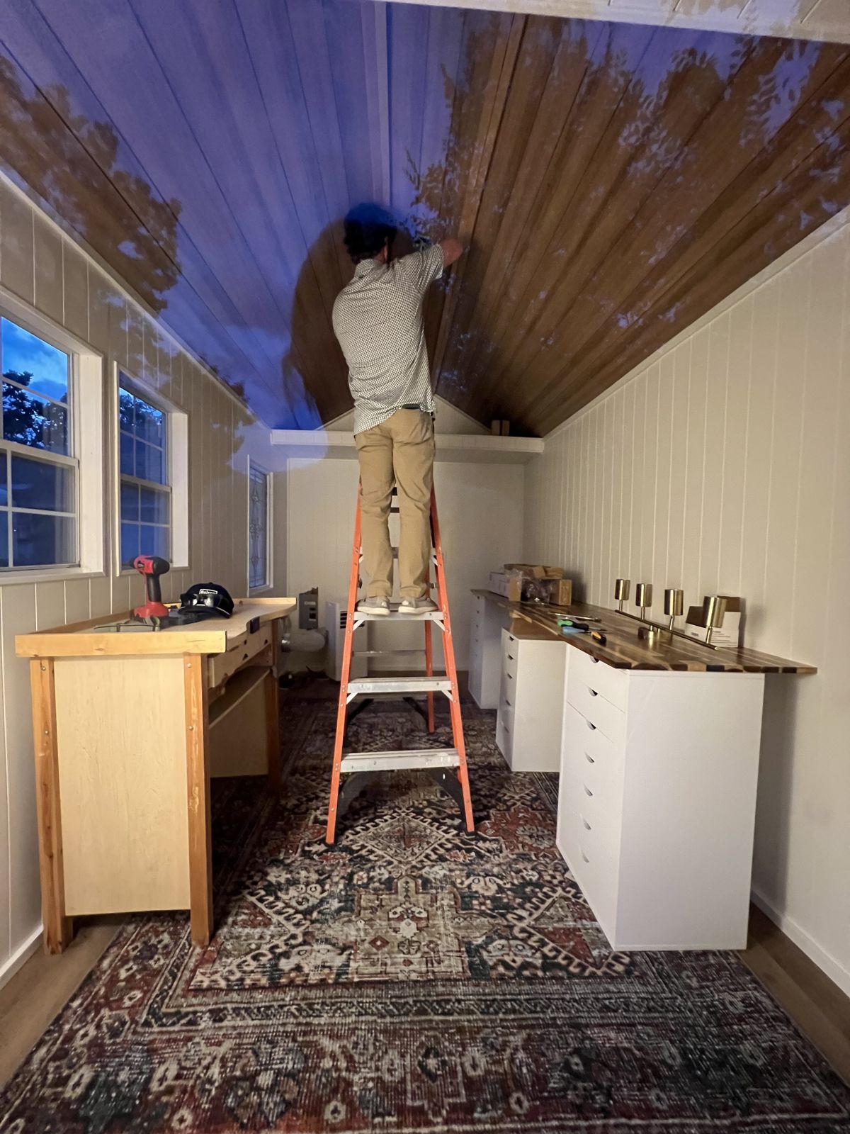 Alex's husband on a ladder working on the studio ceiling in the evening