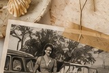 A vintage photograph of a woman leaning on an old car